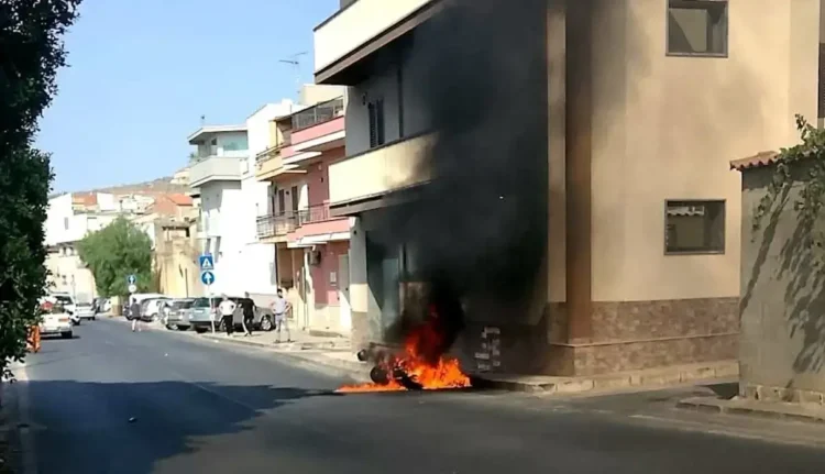 Veicolo in fiamme contro un edificio in una via residenziale di Comiso, con densa colonna di fumo nero che sale verso il cielo