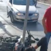 Moto a terra dopo uno scontro con un'auto grigia in strada a Vittoria; un uomo in rosso osserva la scena