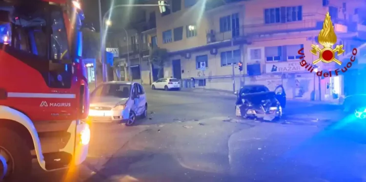 Due auto con i frontali distrutti sull'asfalto di un incrocio notturno a Ragusa, con un mezzo dei Vigili del Fuoco sul lato sinistro.