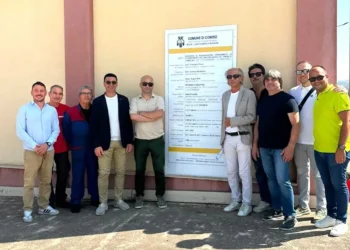 Gruppo di persone in posa davanti al pannello di cantiere del PIP di Comiso, con il logo del Comune di Comiso.