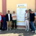 Gruppo di persone in posa davanti al pannello di cantiere del PIP di Comiso, con il logo del Comune di Comiso.