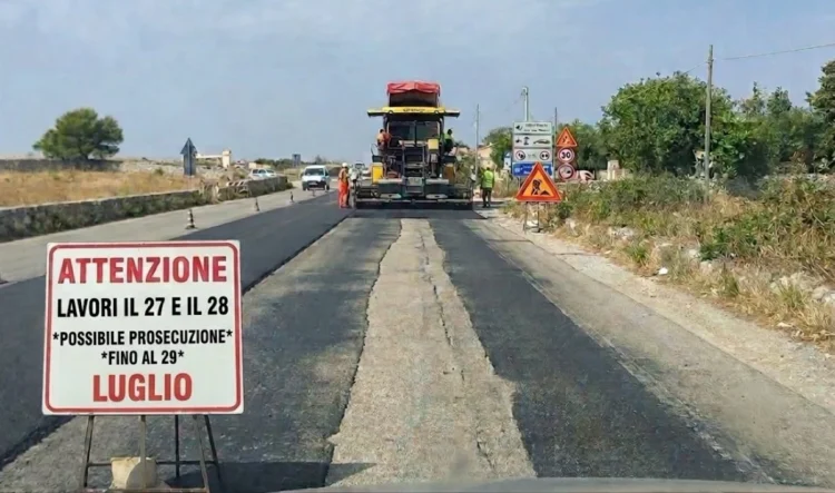 Macchina asfaltrice al lavoro sulla Sp 25 Ragusa-Marina con cartello che annuncia lavori il 27 e 28 luglio, possibile prosecuzione al 29