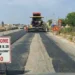 Macchina asfaltrice al lavoro sulla Sp 25 Ragusa-Marina con cartello che annuncia lavori il 27 e 28 luglio, possibile prosecuzione al 29