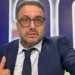 Primo piano del giornalista sportivo Luigi (Luca) Esposito mentre scatta un selfie puntando il pollice verso l'alto davanti a uno sfondo televisivo.