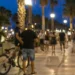 Persone passeggiano sul lungomare di Marina di Ragusa nelle ore serali, mentre un ciclista conduce la bicicletta a mano nell'area pedonale.