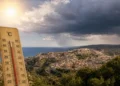 Termometro in primo piano mostra temperature oltre 35°C con panorama di Ragusa Ibla sullo sfondo e nuvole temporalesche
