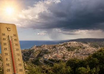Termometro in primo piano mostra temperature oltre 35°C con panorama di Ragusa Ibla sullo sfondo e nuvole temporalesche