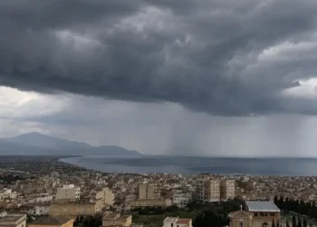 Panoramica di una città siciliana affacciata sul mare con un imponente fronte temporalesco, cielo coperto da nubi scure e piogge visibili in lontananza