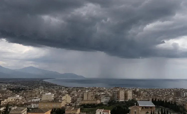 Panoramica di una città siciliana affacciata sul mare con un imponente fronte temporalesco, cielo coperto da nubi scure e piogge visibili in lontananza