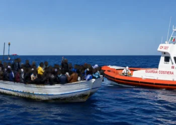 Un'imbarcazione con migranti nel Mediterraneo viene affiancata da una motovedetta della Guardia Costiera durante un'operazione di soccorso. I volti delle persone a bordo sono oscurati per tutelarne la privacy.