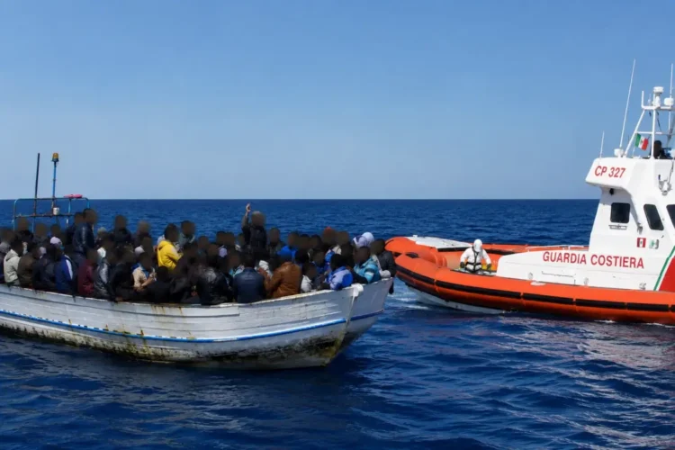 Un'imbarcazione con migranti nel Mediterraneo viene affiancata da una motovedetta della Guardia Costiera durante un'operazione di soccorso. I volti delle persone a bordo sono oscurati per tutelarne la privacy.