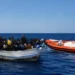Un'imbarcazione con migranti nel Mediterraneo viene affiancata da una motovedetta della Guardia Costiera durante un'operazione di soccorso. I volti delle persone a bordo sono oscurati per tutelarne la privacy.