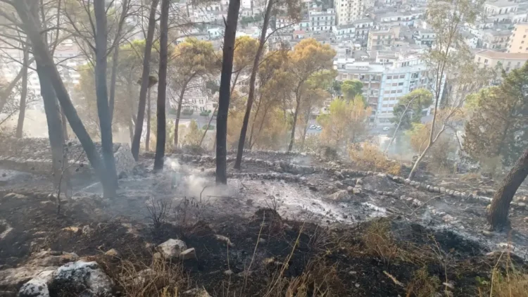 Area boschiva bruciata sulla collina di Monserrato a Modica dopo l'incendio, con focolai in fase di bonifica e la città sullo sfondo