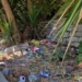Rifiuti sparsi tra la vegetazione nell'area verde del quartiere Dente a Modica, oggetto della denuncia del Movimento 5 Stelle per degrado e mancata manutenzione.