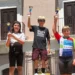 Tre giovani ciclisti sul podio della quarta tappa di ciclismo su strada a Palagonia, con i trofei alzati al termine della gara. Al centro un atleta della Motyka Bike School Modica.