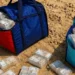 Due borse piene di pacchi di banconote avvolti nel cellophane appoggiate sulla sabbia con altri pacchi sparsi intorno