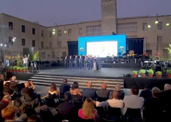 Il palco del Premio Ragusani nel Mondo allestito in Piazza Libertà a Ragusa durante la cerimonia, con il pubblico presente e l'orchestra sullo sfondo.