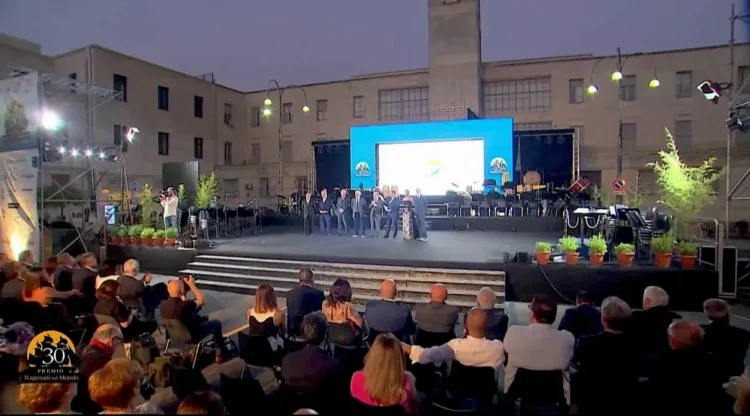 Il palco del Premio Ragusani nel Mondo allestito in Piazza Libertà a Ragusa durante la cerimonia, con il pubblico presente e l'orchestra sullo sfondo.