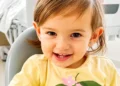 Bambina seduta in un ambiente medico, con un sorriso e una maglietta chiara, durante le cure.