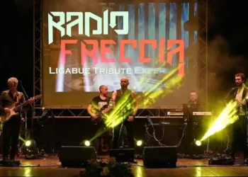 I Radiofreccia sul palco con luci gialle e schermo con il logo della band, durante un concerto all'aperto.