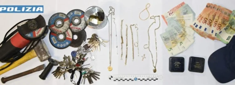 Foto della Polizia di Stato con il materiale sequestrato durante un'indagine per furto in abitazione a Ragusa: banconote in euro, gioielli, mazzi di chiavi, dischi da taglio, martelli, un piede di porco e altri attrezzi da scasso disposti su un tavolo.