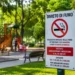 Cartello di divieto di fumo all'ingresso di un'area verde con parco giochi e panchine, a rappresentare la nuova ordinanza del Comune di Ragusa che vieta il fumo nelle aree dedicate ai bambini e allo sport