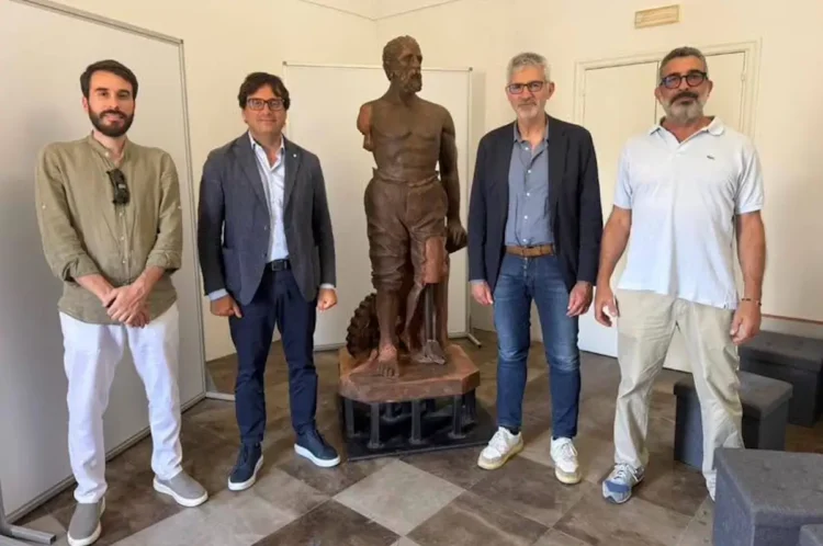 La statua restaurata della Tomba dei Picialuori esposta al Museo della Città di Ragusa, affiancata da quattro persone durante la presentazione del recupero.