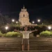 Red Ronnie posa con le braccia aperte sulla scalinata del Duomo di San Giorgio a Modica, illuminato di sera durante la sua vacanza in provincia di Ragusa