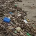 Rifiuti plastici e detriti accumulati sulla sabbia di una spiaggia: bottiglie, taniche e canne intrecciate in un lungo cumulo