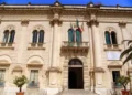 Facciata del Municipio di Scicli con colonne, balcone con bandiere italiana, europea e siciliana, ingresso ad arco