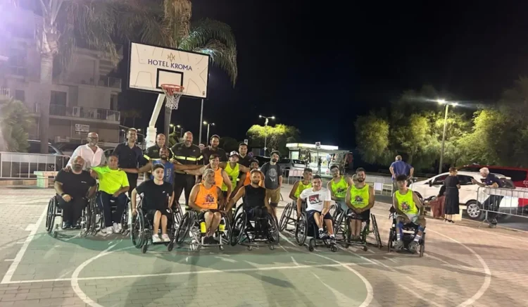 Atleti della Crazy Wheels Ragusa, ospiti e Vigili del Fuoco posano insieme sul campo al termine del torneo Ruote Pazze Ragusa di basket in carrozzina a Marina di Ragusa