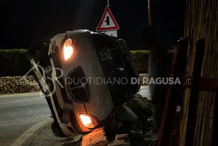 Auto ribaltata su un fianco dopo un incidente sulla strada provinciale Scicli-Sampieri, con il muro di recinzione distrutto dall'impatto.