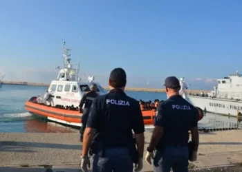 Motovedetta della Guardia Costiera con migranti in arrivo al porto di Pozzallo, mentre agenti della Polizia assistono alle operazioni di sbarco