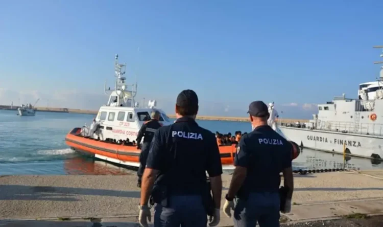 Motovedetta della Guardia Costiera con migranti in arrivo al porto di Pozzallo, mentre agenti della Polizia assistono alle operazioni di sbarco