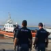 Motovedetta della Guardia Costiera con migranti in arrivo al porto di Pozzallo, mentre agenti della Polizia assistono alle operazioni di sbarco