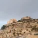 Veduta panoramica del colle di San Matteo a Scicli con l'antica chiesa sulla sommità e il centro storico ai piedi della collina sotto un cielo nuvoloso