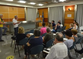Riunione di medici di famiglia in una sala istituzionale con bandiere italiana ed europea, due relatori in piedi davanti ai presenti
