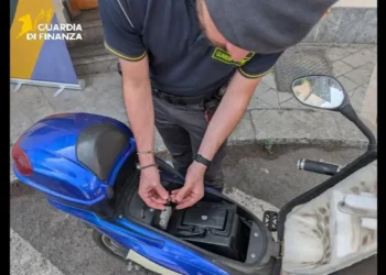 Un finanziere esamina i componenti elettrici interni di uno scooter blu durante un'operazione di sequestro