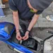 Un finanziere esamina i componenti elettrici interni di uno scooter blu durante un'operazione di sequestro