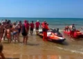 Operatori in divisa rossa con moto d'acqua e kayak di salvataggio sulla riva durante una simulazione di soccorso in mare.