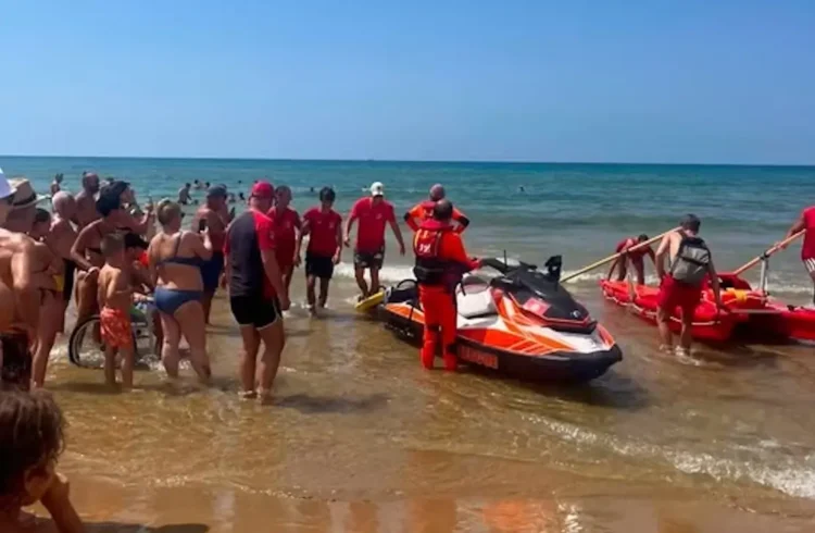Operatori in divisa rossa con moto d'acqua e kayak di salvataggio sulla riva durante una simulazione di soccorso in mare.