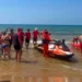 Operatori in divisa rossa con moto d'acqua e kayak di salvataggio sulla riva durante una simulazione di soccorso in mare.