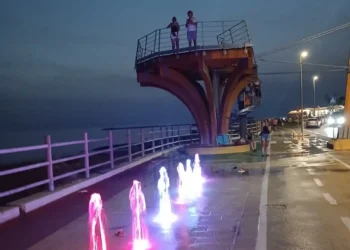 La Skyview di Scoglitti di notte: due persone sulla piattaforma panoramica, davanti giochi d'acqua colorati sul lungomare.