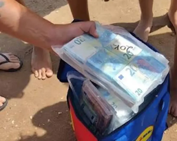 Mazzette di banconote da 20 euro in sacchetti di plastica trasparenti estratti da una borsa frigo colorata su una spiaggia