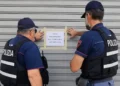 Due agenti di polizia in giubbotto antiproiettile applicano un cartello di chiusura su una serranda metallica.