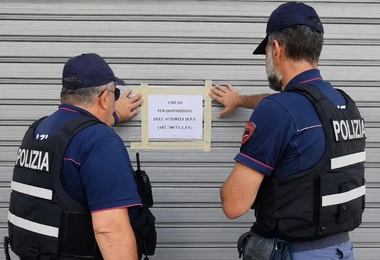 Due agenti di polizia in giubbotto antiproiettile applicano un cartello di chiusura su una serranda metallica.