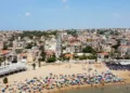 Vista aerea della spiaggia di Marina di Ragusa con bagnanti, ombrelloni colorati e il centro abitato sullo sfondo.
