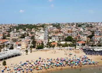Vista aerea della spiaggia di Marina di Ragusa con bagnanti, ombrelloni colorati e il centro abitato sullo sfondo.