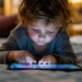 Bambino molto piccolo sdraiato su un letto mentre utilizza un tablet, immagine rappresentativa dell'esposizione precoce ai dispositivi digitali.