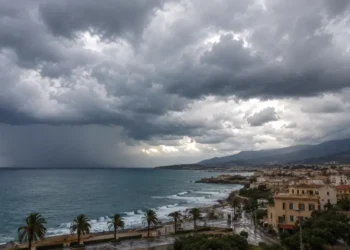 Nuvole temporalesche su un centro costiero siciliano con mare mosso, cortina di pioggia all'orizzonte e palme piegate dal vento.